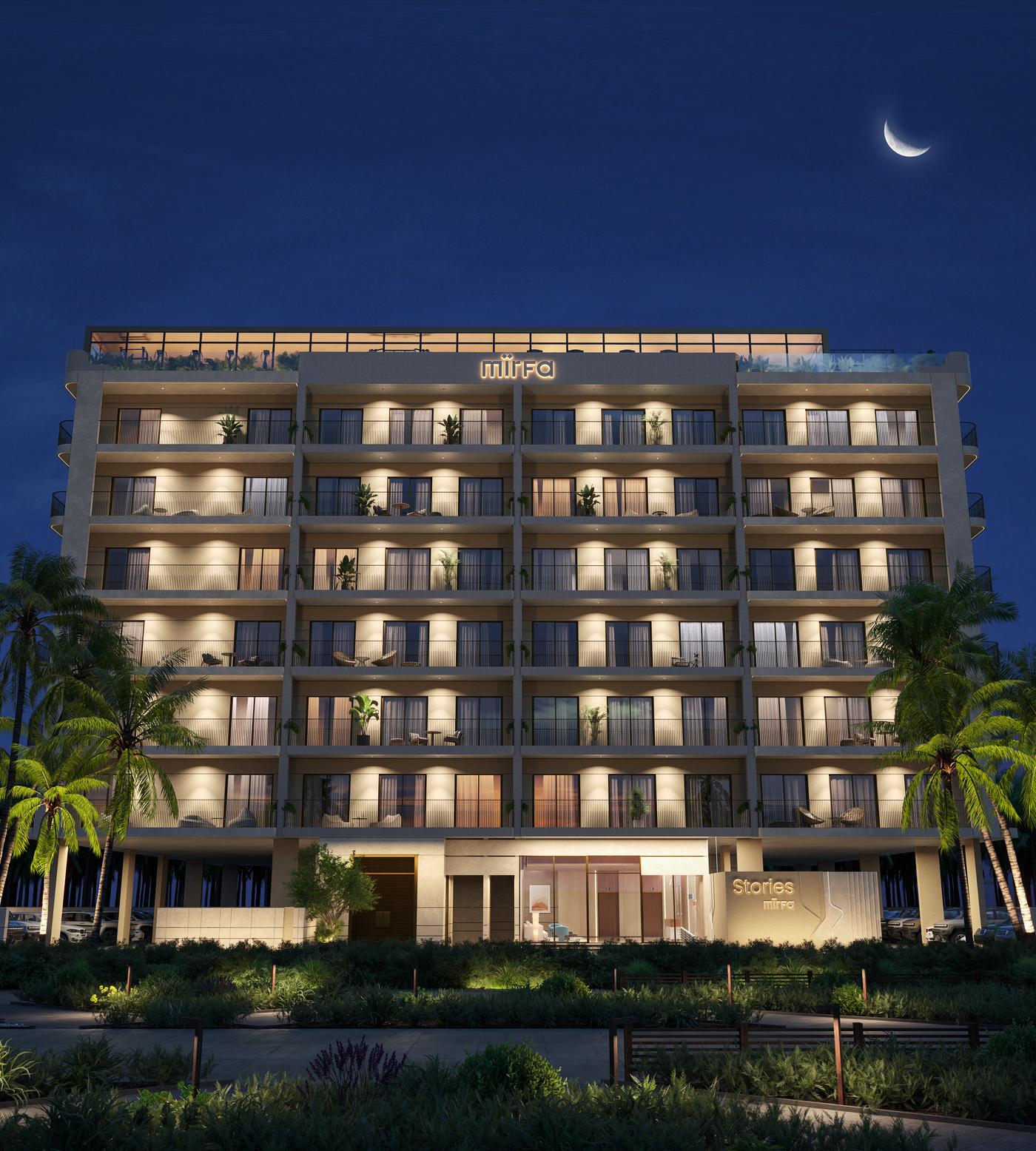 Night-time render of the Stories by Mirfa building: a seven-storey apartment block with lit balconies, palm trees and a rooftop terrace